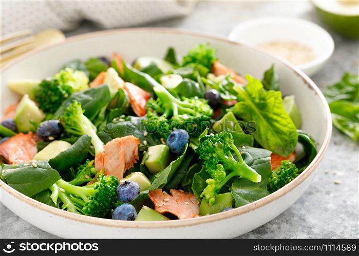 Salmon fish and avocado salad with fresh spinach leaves, broccoli, blueberry dressed with olive oil