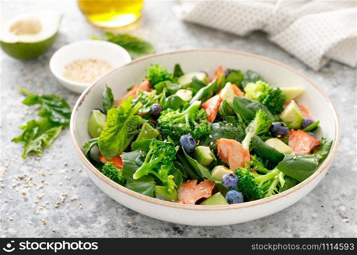 Salmon fish and avocado salad with fresh spinach leaves, broccoli, blueberry dressed with olive oil