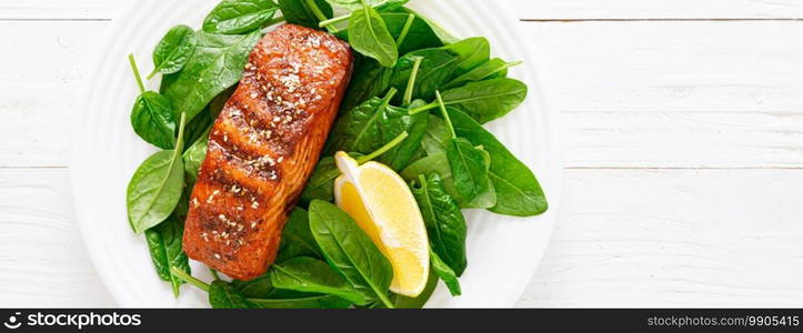 Salmon fish fillet grilled and fresh spinach salad on plate for lunch. Top view. Banner