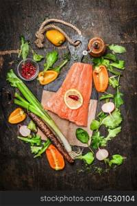 Salmon fish fillets on cutting board with fresh vegetables and spices ingredients on rustic wooden background, top view. Healthy clean food or diet cooking concept.