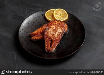 Salmon fish steak cooked. Dinner seafood dish plate. Grilled salmon with lemon, delicious lunch. Isolated roast fish portion, healthy bbq recipe, restaurant cuisine. Crispy norwegian salmon, dark, top. Salmon fish steak cooked Dinner seafood dish plate