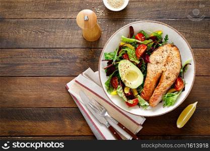 Salmon fish steak grilled, avocado and fresh vegetable salad with tomato, bell pepper and leafy vegetables. Top view