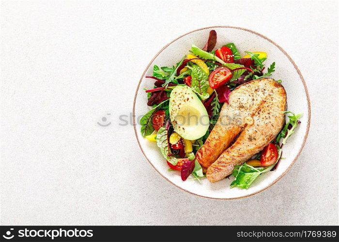 Salmon fish steak grilled, avocado and fresh vegetable salad with tomato, bell pepper and leafy vegetables, top view.