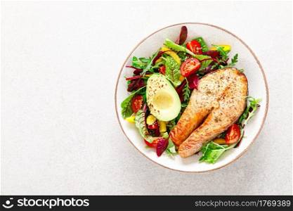Salmon fish steak grilled, avocado and fresh vegetable salad with tomato, bell pepper and leafy vegetables, top view.