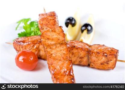 salmon kebab at plate with green lettuce and lemon on a white