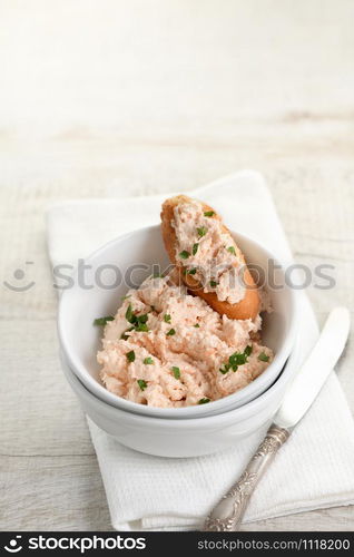 Salmon paste bowl with soft cheese and herb, toasted sliced ??bread, vintage knife with a textile napkin on a wooden table