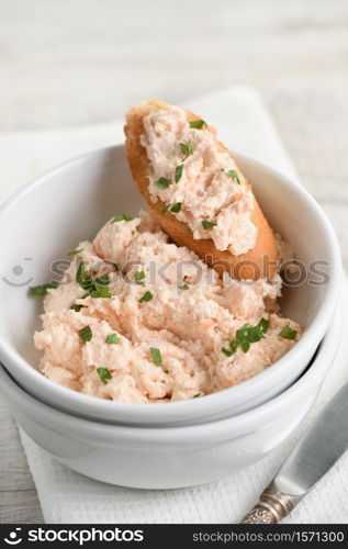 Salmon paste bowl with soft cheese and herb, toasted sliced ??bread, vintage knife with a textile napkin on a wooden table