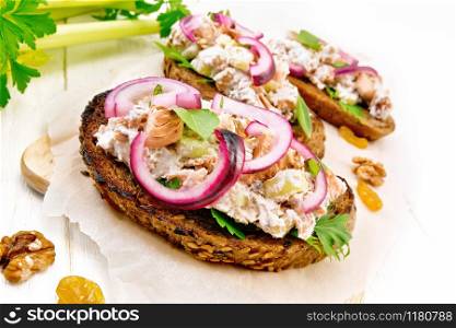Salmon, petiole celery, raisins, walnuts, red onions and curd cheese salad on toasted bread with green lettuce leaves on parchment on a light wooden board background