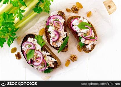 Salmon, petiole celery, raisins, walnuts, red onions and curd cheese salad on toasted bread with green lettuce on paper on a wooden board background from above