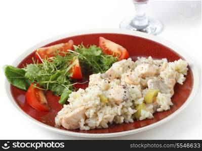 Salmon risotto, dusted with pepper, on a plate with a leafy salad and tomatoes.