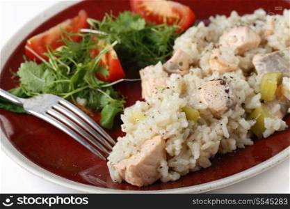Salmon risotto on a plate with a leafy salad and tomatoes,