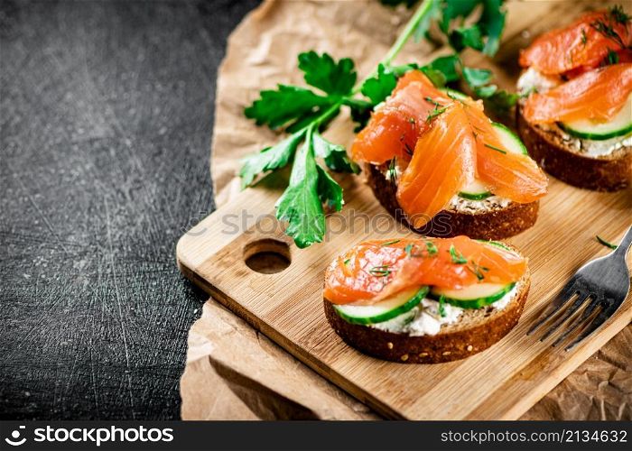 Salmon sandwich on a cutting board. On a black background. High quality photo. Salmon sandwich on a cutting board.