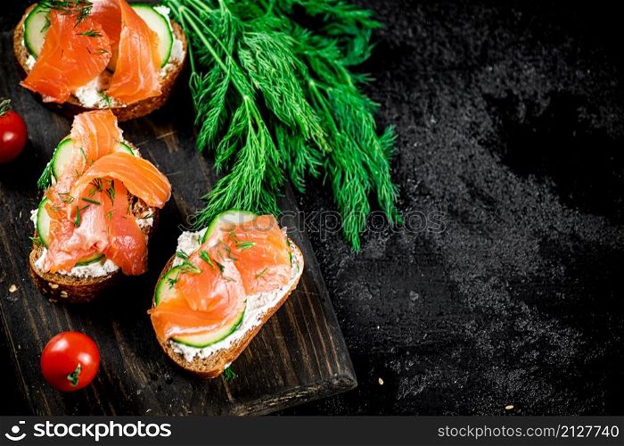 Salmon sandwich on a cutting board with herbs and tomatoes. On a black background. High quality photo. Salmon sandwich on a cutting board with herbs and tomatoes.