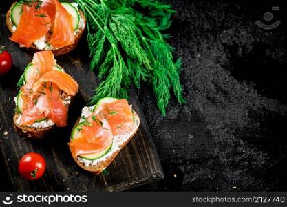 Salmon sandwich on a cutting board with herbs and tomatoes. On a black background. High quality photo. Salmon sandwich on a cutting board with herbs and tomatoes.