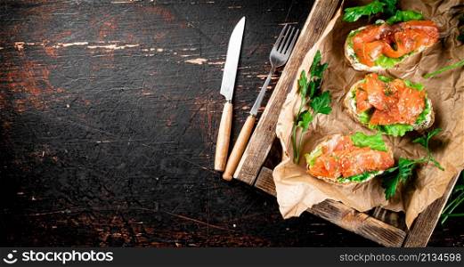 Salmon sandwich on a wooden tray. Against a dark background. High quality photo. Salmon sandwich on a wooden tray.
