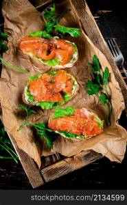 Salmon sandwich on a wooden tray. Against a dark background. High quality photo. Salmon sandwich on a wooden tray.