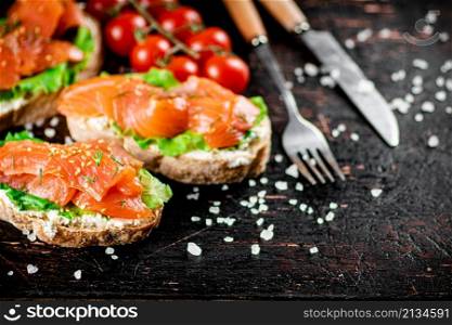 Salmon sandwich on the table with tomatoes and salt. On a rustic dark background. High quality photo. Salmon sandwich on the table with tomatoes and salt.