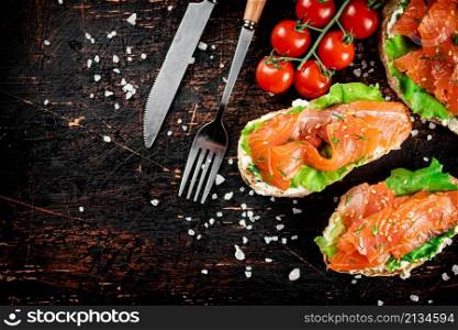 Salmon sandwich on the table with tomatoes and salt. On a rustic dark background. High quality photo. Salmon sandwich on the table with tomatoes and salt.