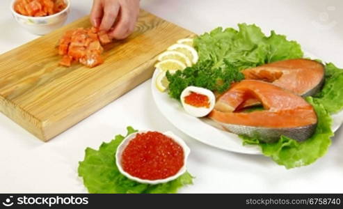 Salmon steak and red caviar, In the background female cutting fish steak