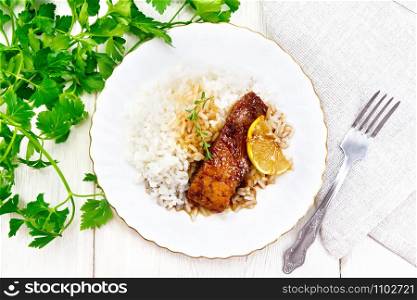 Salmon with sauce of honey, lemon juice, garlic, hot pepper and soy sauce, boiled rice, lemon and thyme in a plate, parsley, towel and fork on the background of wooden board on top. Salmon with sauce in plate on white board top