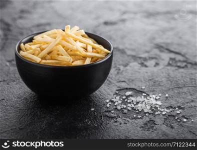Salt and vinegar potato sticks in white bowl, classic snack on black kitchen table.
