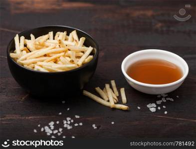 Salt and vinegar potato sticks in white bowl, classic snack with ketchup on wood.