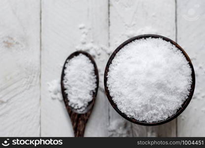 Salt in a cup is placed on a white wooden table.