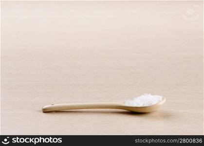 Salt in a spoon over a blured wooden background with copy space