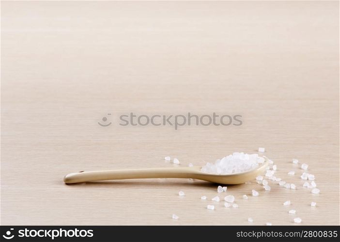 Salt in a spoon with some spilt over the wooden background with copy space