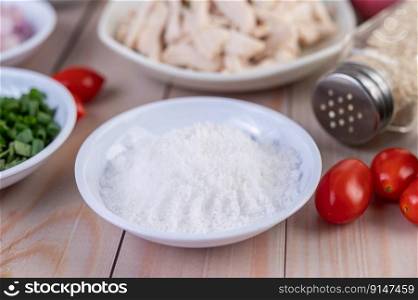 Salt in a white spoon, tomatoes placed on a wooden table. Selective focus.