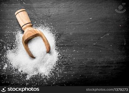 Salt in a wooden scoop. On the black chalkboard.. Salt in a wooden scoop.