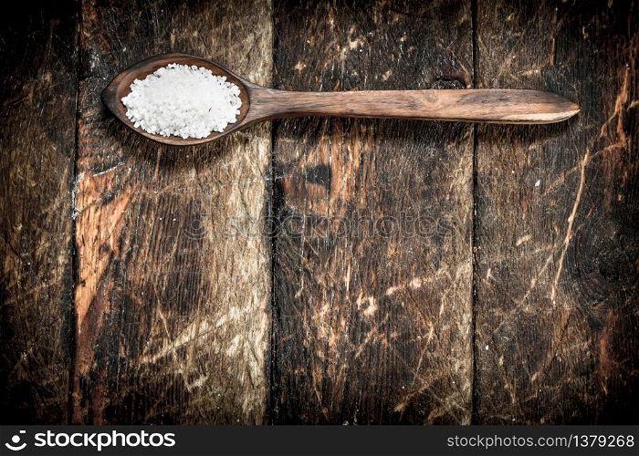 Salt in a wooden spoon. On wooden background.. Salt in a wooden spoon.