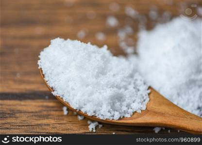 Salt in wooden spoon and heap of white salt on background
