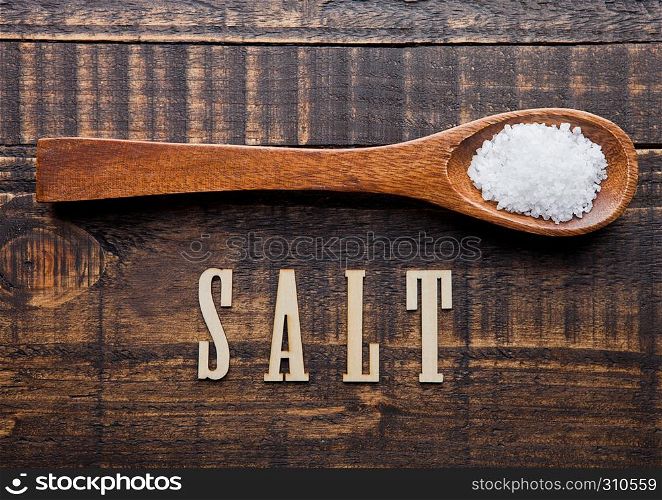 Salt on wooden spoon and grunge wooden plate with letters below