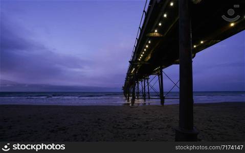 Saltburn pier in winter with dramatic sky in evening, Saltburn is a seaside town located on the northeast coast of the UK, Perspective of wooden bridge to the sea with reflection of light under