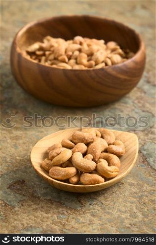 Salted cashew nuts or seeds on small bamboo plate, photographed on slate with natural light (Selective Focus, Focus one third into the image)