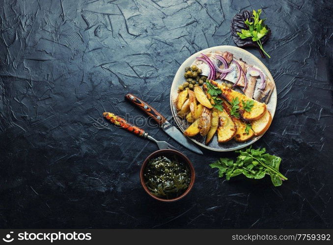 Salted herring fish with roasted potatoes on the plate.Copy space. Salted herring with baked potatoes