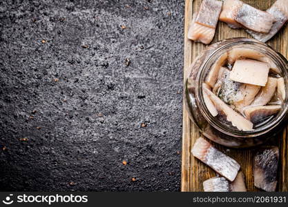 Salted herring in a glass jar on a cutting board. On a black background. High quality photo. Salted herring in a glass jar on a cutting board.