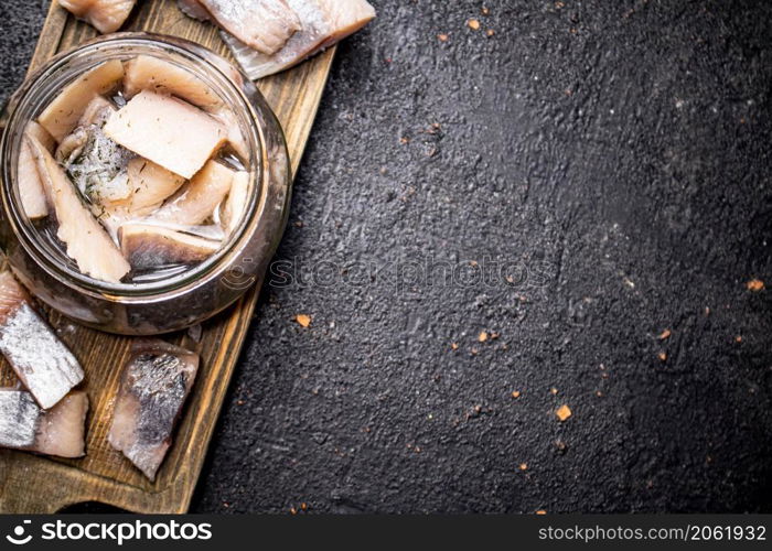Salted herring in a glass jar on a cutting board. On a black background. High quality photo. Salted herring in a glass jar on a cutting board.