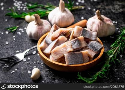Salted herring on a wooden plate with garlic and rosemary. On a black background. High quality photo. Salted herring on a wooden plate with garlic and rosemary.
