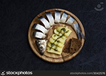 Salted herring with boiled potatoes and green sauce.. Salted herring with boiled potatoes and green sauce on a dark background.