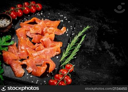 Salted salmon on a stone board with tomatoes and greens. On a black background. High quality photo. Salted salmon on a stone board with tomatoes and greens.