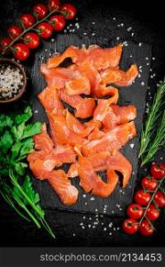 Salted salmon on a stone board with tomatoes and greens. On a black background. High quality photo. Salted salmon on a stone board with tomatoes and greens.