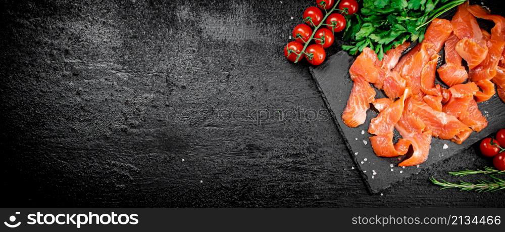 Salted salmon on a stone board with tomatoes and greens. On a black background. High quality photo. Salted salmon on a stone board with tomatoes and greens.