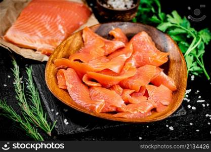 Salted salmon on a wooden plate with greens. On a black background. High quality photo. Salted salmon on a wooden plate with greens.