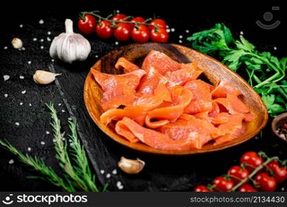 Salted salmon on a wooden plate with greens. On a black background. High quality photo. Salted salmon on a wooden plate with greens.
