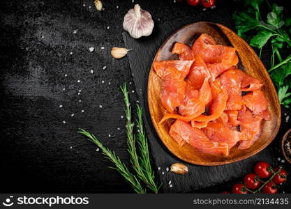 Salted salmon on a wooden plate with greens. On a black background. High quality photo. Salted salmon on a wooden plate with greens.