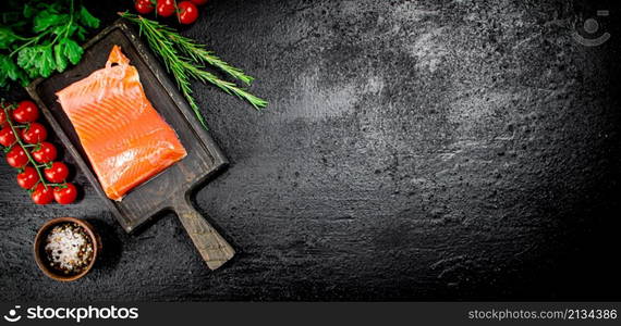 Salted salmon with greens and tomatoes on a cutting board. On a black background. High quality photo. Salted salmon with greens and tomatoes on a cutting board.