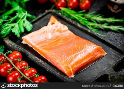 Salted salmon with greens and tomatoes on a cutting board. On a black background. High quality photo. Salted salmon with greens and tomatoes on a cutting board.