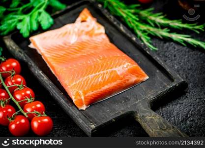Salted salmon with greens and tomatoes on a cutting board. On a black background. High quality photo. Salted salmon with greens and tomatoes on a cutting board.